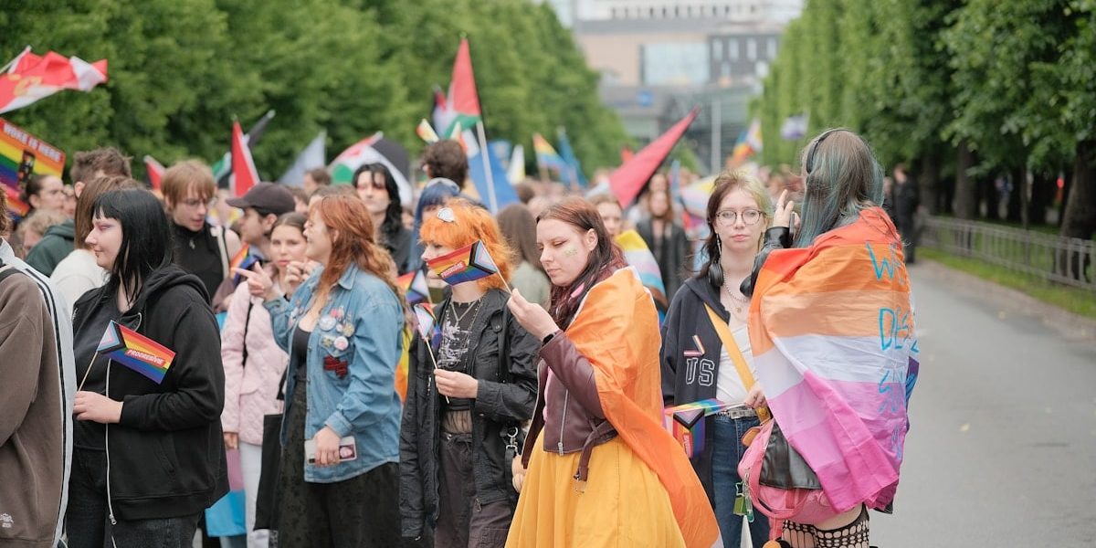 Diverse crowd marching with pride flags in a street parade.