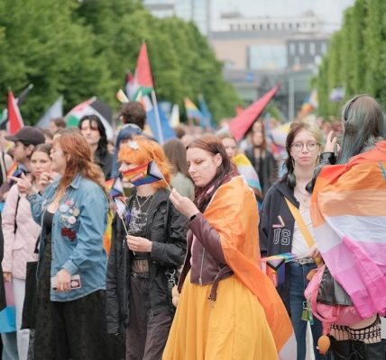 Diverse crowd marching with pride flags in a street parade.