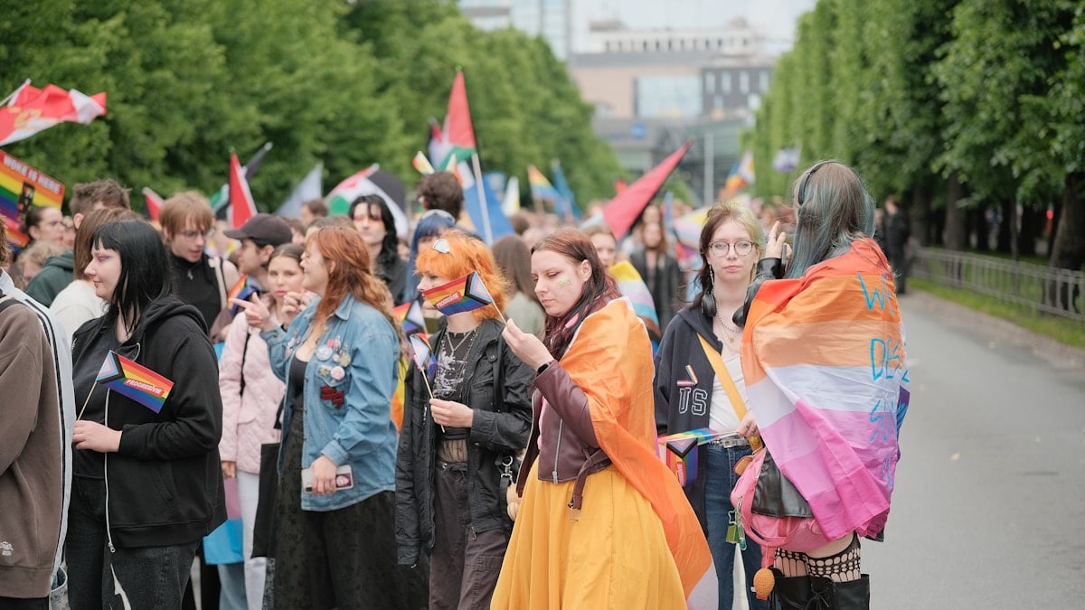 Diverse crowd marching with pride flags in a street parade.